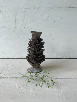 Candelabro di metallo a forma di pigna. La base è piccola e rotonda, con un corpo che si allarga in strati sovrapposti simili a quelli di una pigna, culminando in un portacandele stretto in cima.