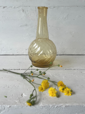 Vaso piccolo ocra, base arrotondata e collo stretto e lungo che termina con un'apertura leggermente svasata. Superficie con leggere scanalature diagonali sulla base.